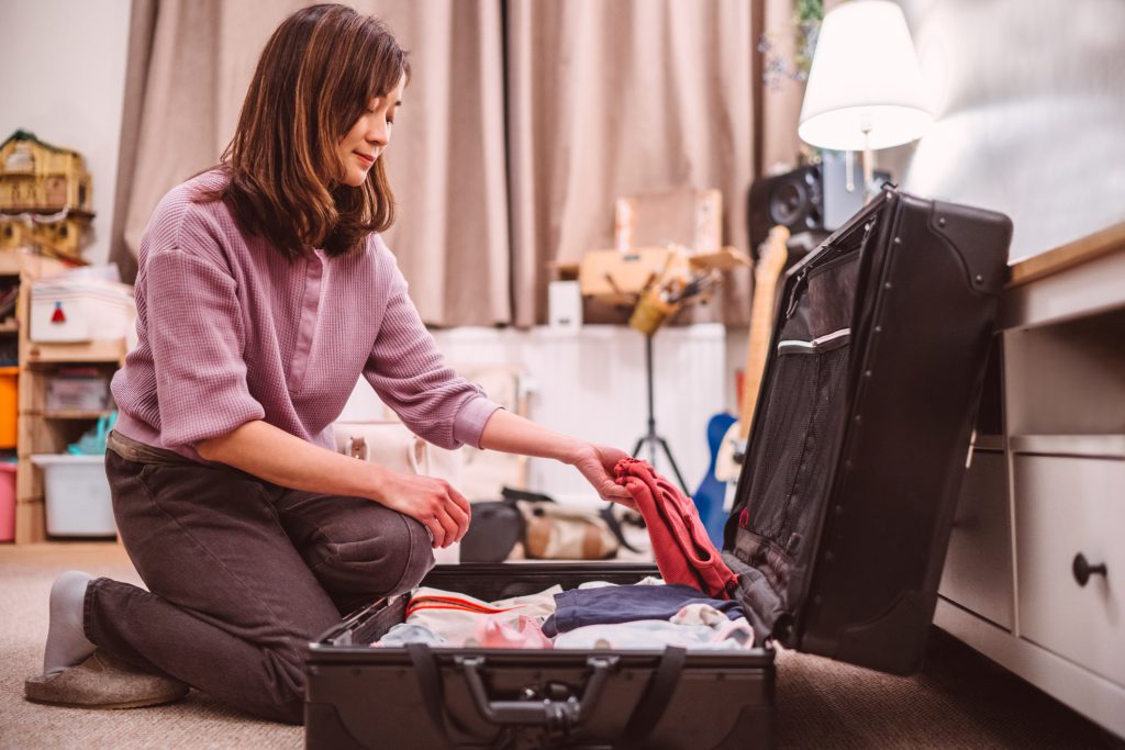 Young Asian woman packing a suitcase for trip at home.